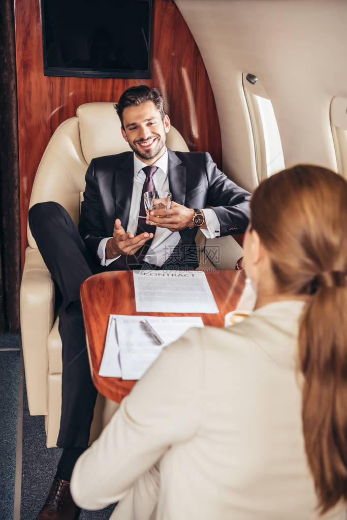 在私人飞机上与商业女商人交谈的有玻璃质的商图片