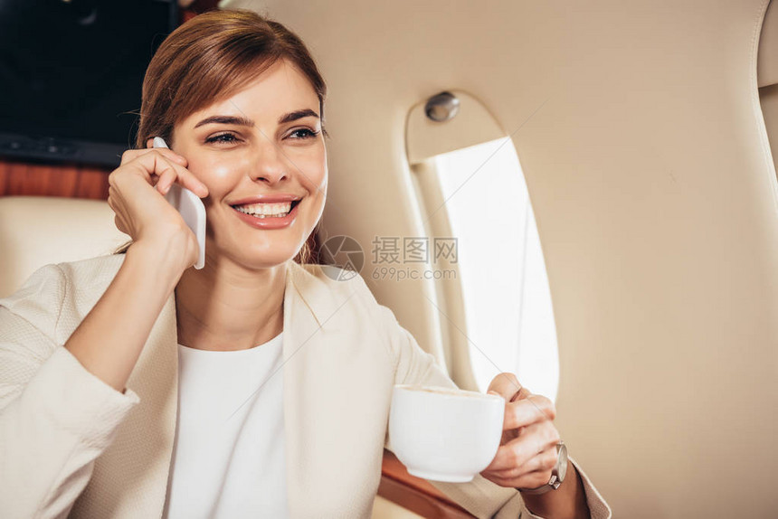 穿着西装拿着杯子和在私人飞机上用智能手机说话图片