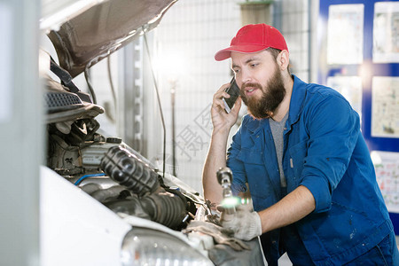 机器维修服务的留着胡子的年轻工人站在破车发动机旁图片