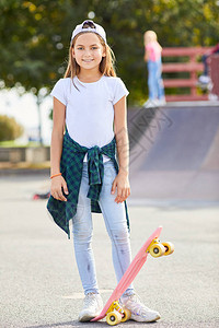 穿着牛仔裤和帽子的可爱女孩肖像与滑板站在一起图片