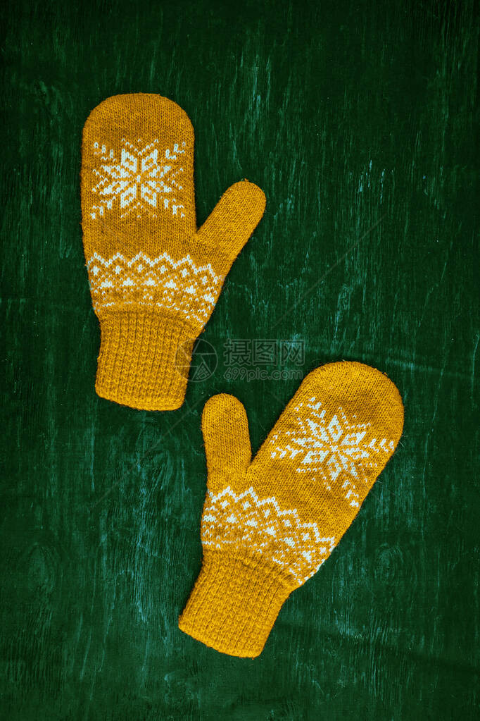 一对黄色橙编织的手套印在深蓝色绿褐木质古董背景图片