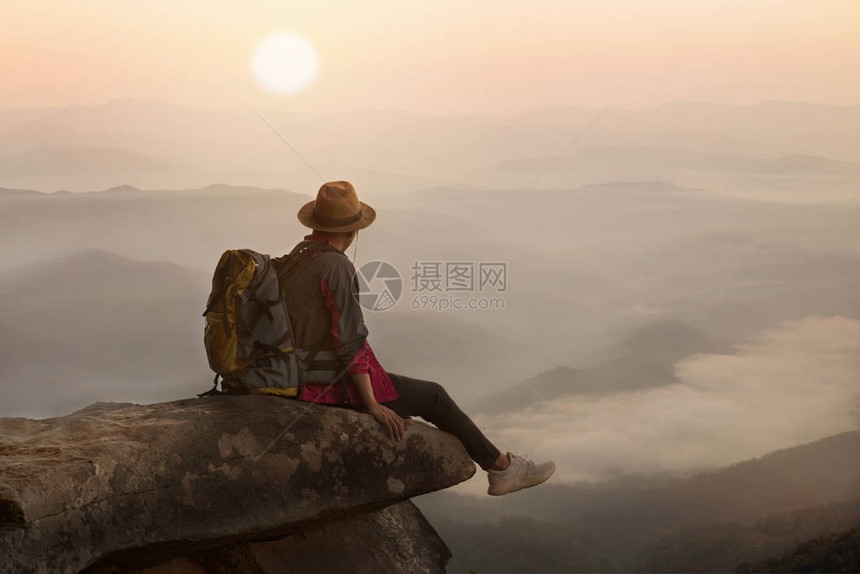 背包客坐在日落背景的悬崖上图片