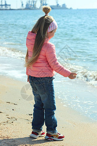 一个长着金色长发的小女孩在沙滩上玩着沙子和贝壳图片