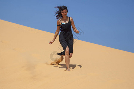 沙漠中美丽的女孩赤脚跑在山顶的沙丘上自由的概图片