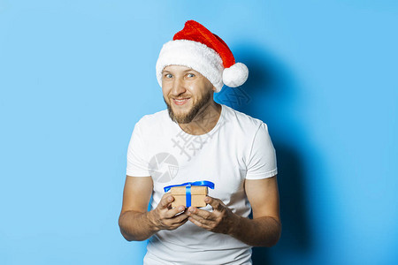 戴着圣诞老人帽子的男人拿着蓝色背景的礼物图片