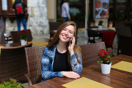 年轻的高加索女在红花附近的咖啡馆用智能手机说话现代技术的概念和有图片