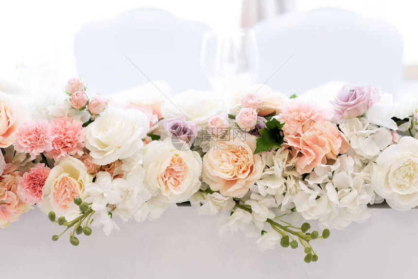 一束美丽的花束放在由不同色调的玫瑰制成的细长婚礼桌上白色背景图片