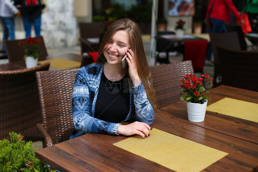女青年在咖啡馆的红花附近用智能手机讲话图片