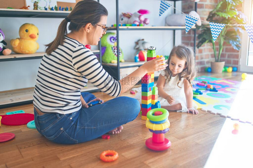 美丽的女教师和幼童在幼儿园里玩许多玩具的建筑砖块图片