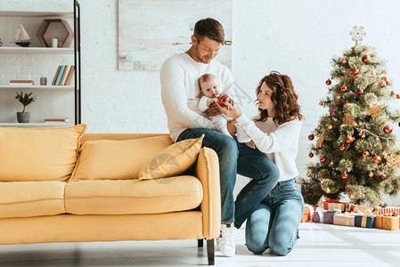 有魅力的女子将圣诞节舞会送给婴儿坐在父亲双手上在受装图片