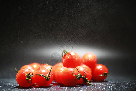 喷雾中黑色背景中的樱桃番茄图片