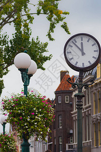 以鲜花和绿色灯柱为背景的街钟图片