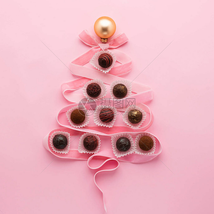来自各种巧克力的巧克力和粉红色的天鹅绒丝带以粉红色背景上的圣诞树形状布置新年假期概图片