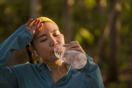 年轻的亚洲跑步女孩喝水汗流浃背图片