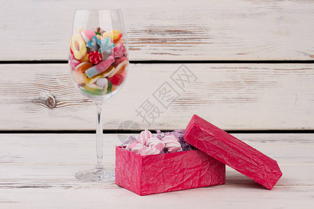 葡萄酒杯彩色糖果和装满棉花糖的粉红色盒子图片