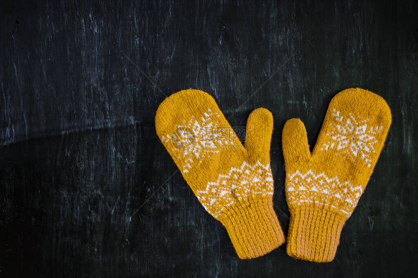 一对黄色橙编织的手套印在深蓝色绿褐木质古董背景图片