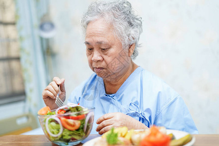 亚洲老年或老年妇人患者在医院病床上坐着饥饿时满怀希望和快乐地吃图片