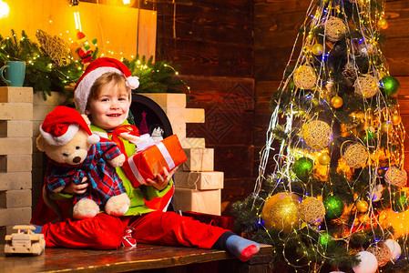 快乐微笑的小男孩拿着他的泰迪熊和圣诞礼物靠近壁炉和装饰树小男孩装饰圣诞背景图片