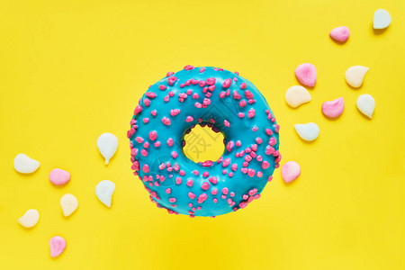 洒了蓝色甜圈上釉洒甜圈在明亮的黄色背景与五颜六色的糖果顶视图片