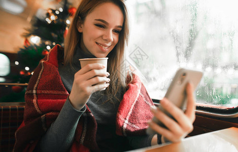可爱的女孩在寒冷的冬日在圣诞树背景下的舒适咖啡馆里度过休闲时光图片