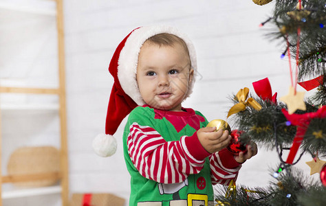 穿着圣诞老人帮手服装的婴儿在家中装饰圣图片
