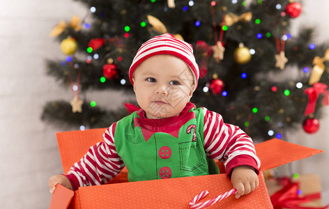 好奇的婴儿在Xmas树下的大盒子里寻找圣诞礼图片
