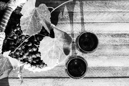 两杯红葡萄酒和一篮子葡萄放在日光天日最佳景色的木制背景图片
