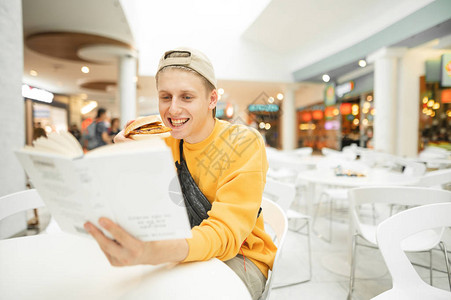 手里拿着汉堡的快乐男孩坐在白桌旁的一家餐馆里图片