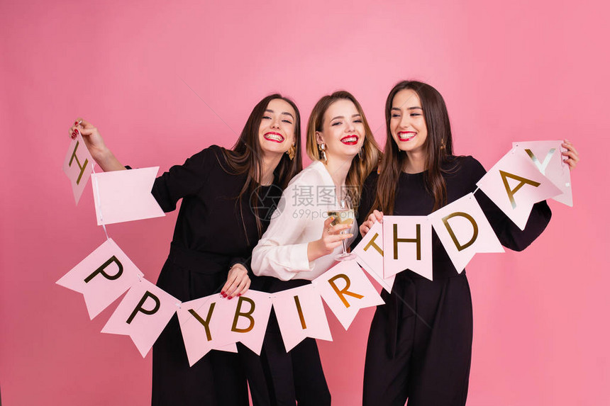 三个美丽优雅的女人庆祝生日聚会和喝鸡尾酒最好的朋友穿着黑色和白色时尚的晚装与花环与生日快乐题字亮妆图片