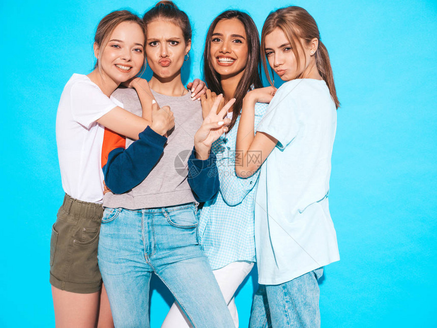 四个年轻漂亮的微笑时髦女孩穿着时髦的夏装在工作室的蓝色墙壁附近摆姿势的感无忧虑的女人快乐和拥图片