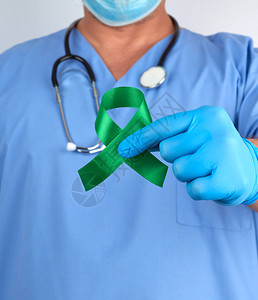 身穿蓝色制服和乳胶手套的医生拿着一条绿丝带图片