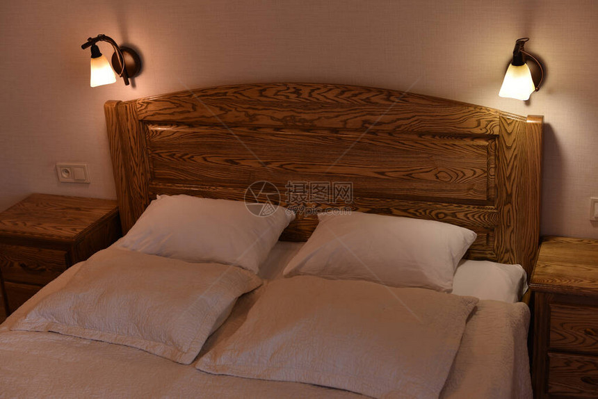 酒店房间的床和枕头一张带木制床头板和两个橱柜和落地灯的床白天或晚上的酒店睡觉和放松的地方白色枕套中图片