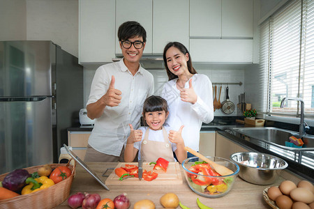 亚洲家庭与父亲母亲和女儿一起在家里的厨房做饭时切碎蔬菜沙拉并大呼过瘾图片