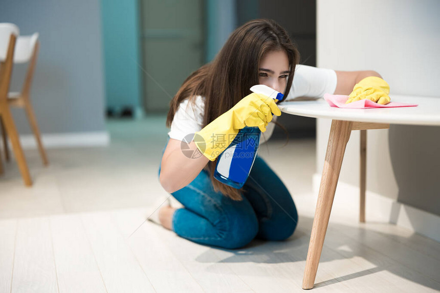 穿着黄色手套的可爱年轻女人手掌里有洗涤剂喷雾在厨房椅子上用图片