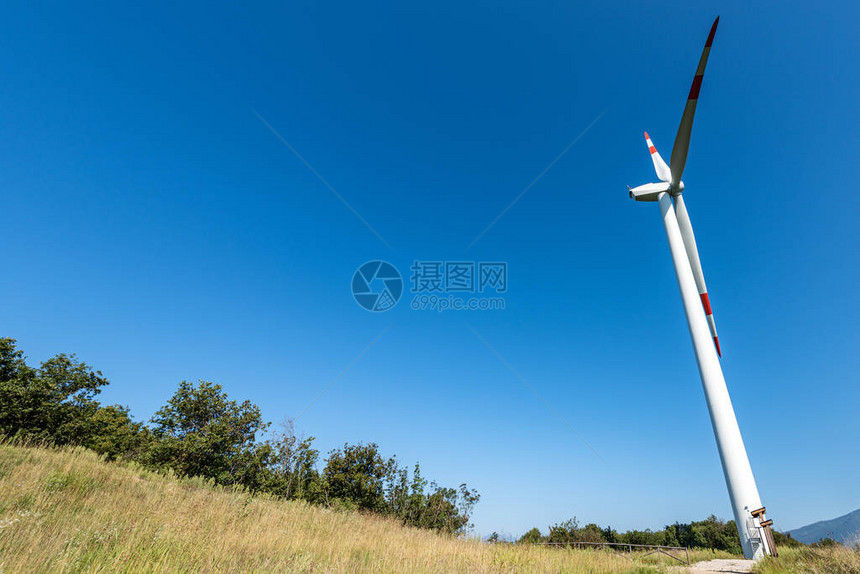 位于明蓝天空上山丘之上的白色和红色风力涡轮机图片