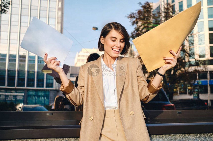 年轻快乐的女商人拿着信封在街上反图片