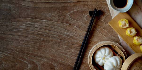 竹蒸笼中的国蒸饺和蒸猪肉包木桌上有筷子图片