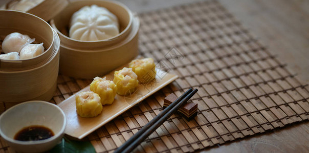 竹蒸笼中的国蒸饺和蒸猪肉包木桌上有筷子图片