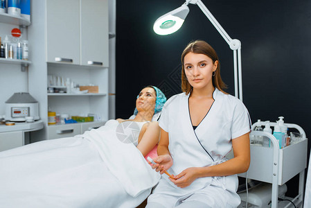 美容师用刷子坐在治疗台上的女病人附近在美容院的复兴程序医生和女人图片