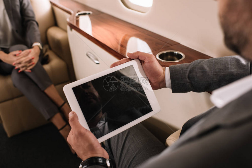 在私人喷气式飞机上与同事相近处持有带空白屏幕的数字平板电脑的商图片