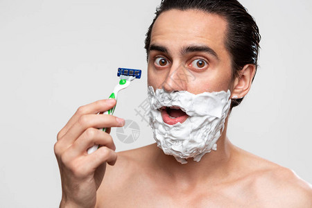 留着小胡子的英俊男人使用剃须棒和剃须泡沫来修剪他的胡须图片