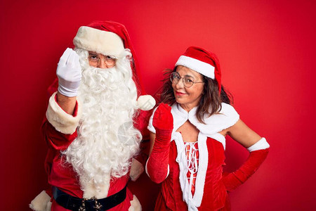 中年夫妇在孤立的红色背景中穿着圣诞老人服装和眼镜图片