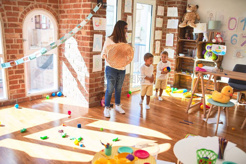 漂亮的老师和幼儿在幼儿园的许多玩具周围用球和图片