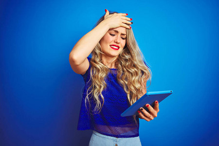 年轻漂亮的女人在蓝色孤立的背景下使用平板电脑图片