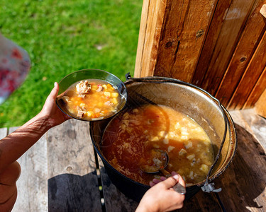 在户外做饭的女孩把肉汤和蔬菜罗宋汤从一个大锅里放在房子的木地板上图片