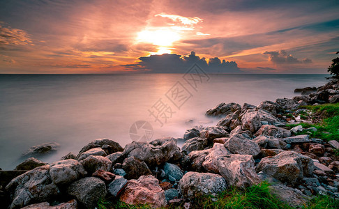 日落时在石滩上的岩石平静的海面美丽的风景黄昏的热带海戏剧夕阳天空和云彩自然之美宁静祥和的概念干背景图片