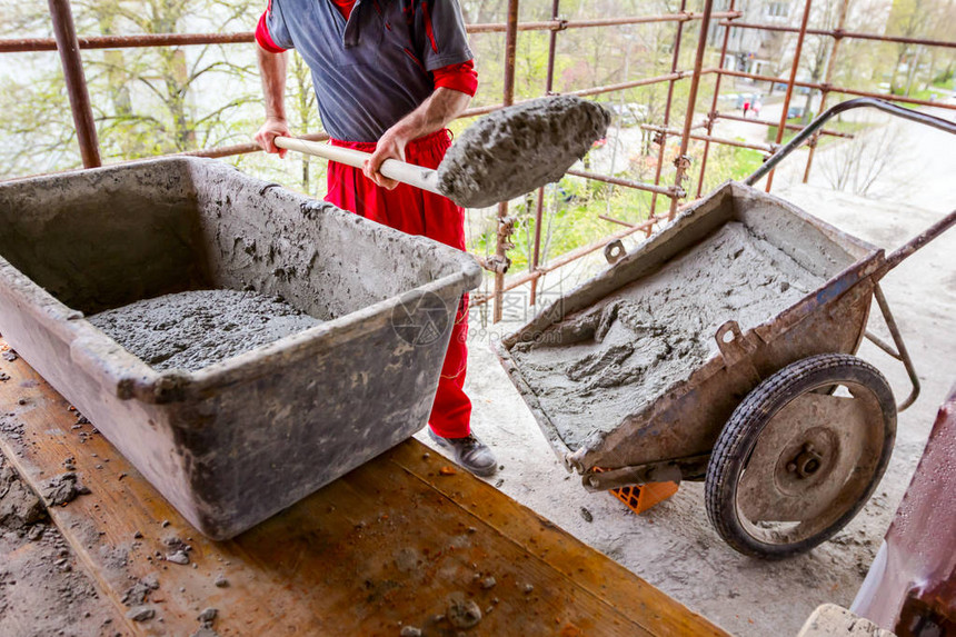 建筑工人正在用铲子从建筑工地的手推车上卸下图片