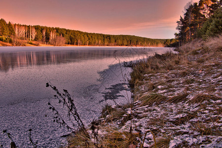 冬季森林的日落结冰的河岸上的森林河上的图片