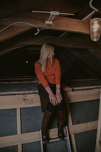 穿着橙色毛衣和皮靴的金发美女坐在衣服上木图片