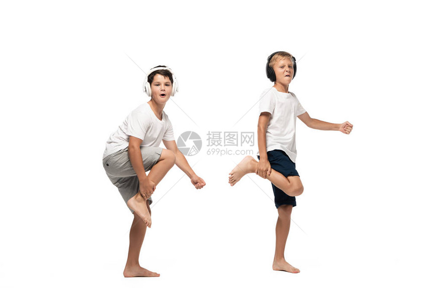 两个快乐的兄弟在看镜头和用耳机跳舞在白色图片